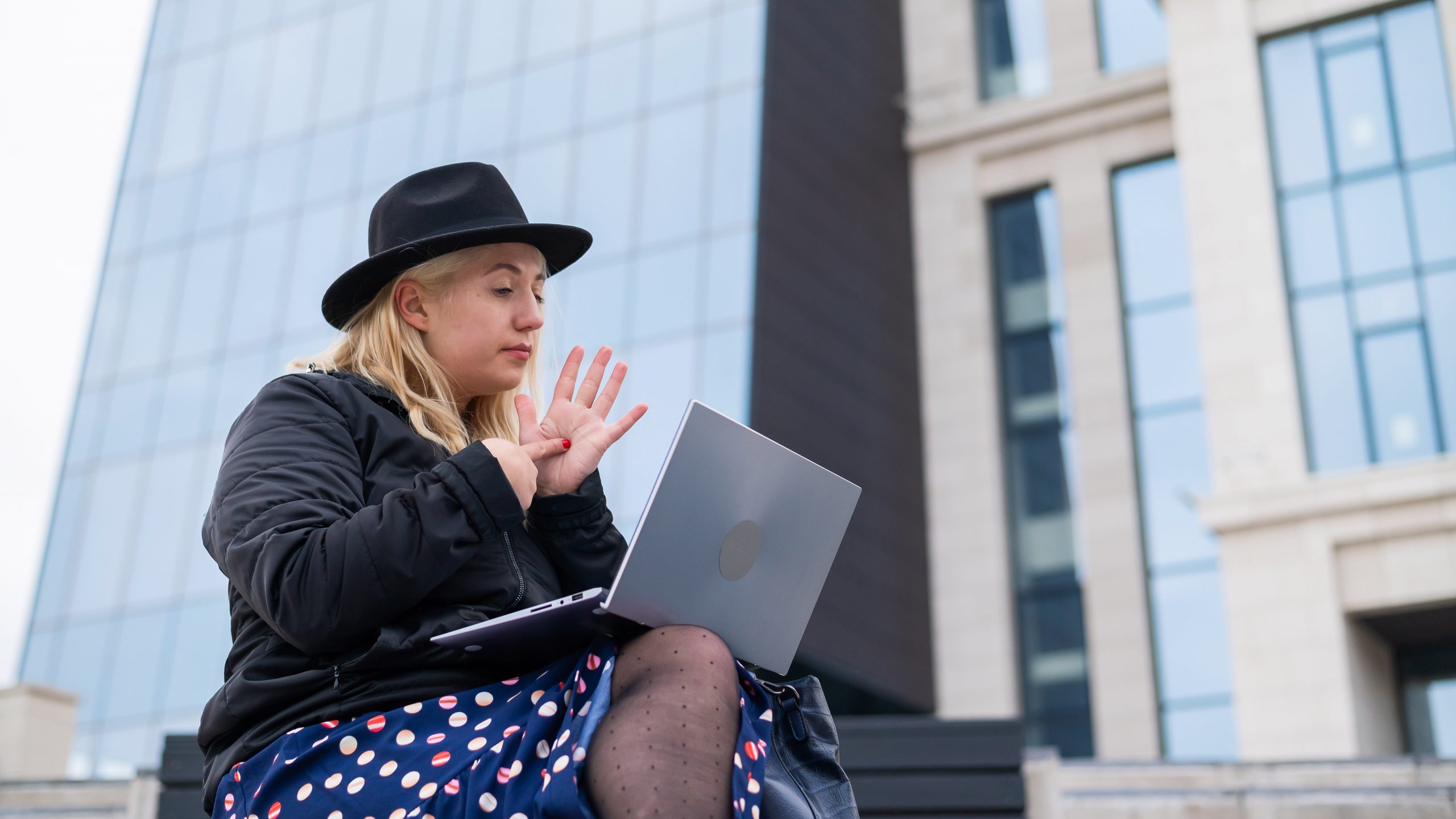 Young woman speaks sign language on a video call on a laptop outdoors. The deaf-mute girl communicates with gestures
