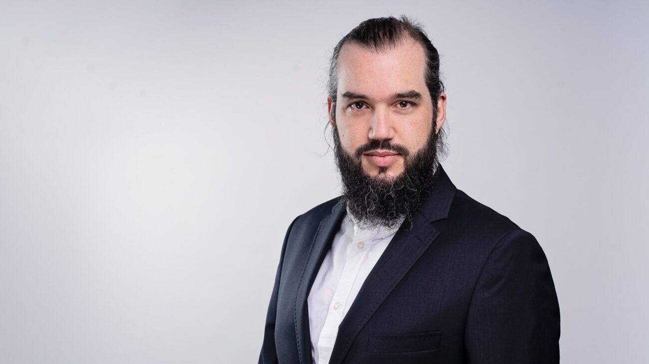 Na zdjęciu widzimy Marcina Przygórzewskiego - analityka serwisu Walutomat. Czarne włosy, długa broda. Mężczyzna nosi garnitur i białą koszulę bez dodatków
